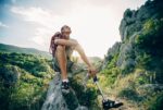A man with a prosthetic leg sitting on top of a rock after rock climbing.