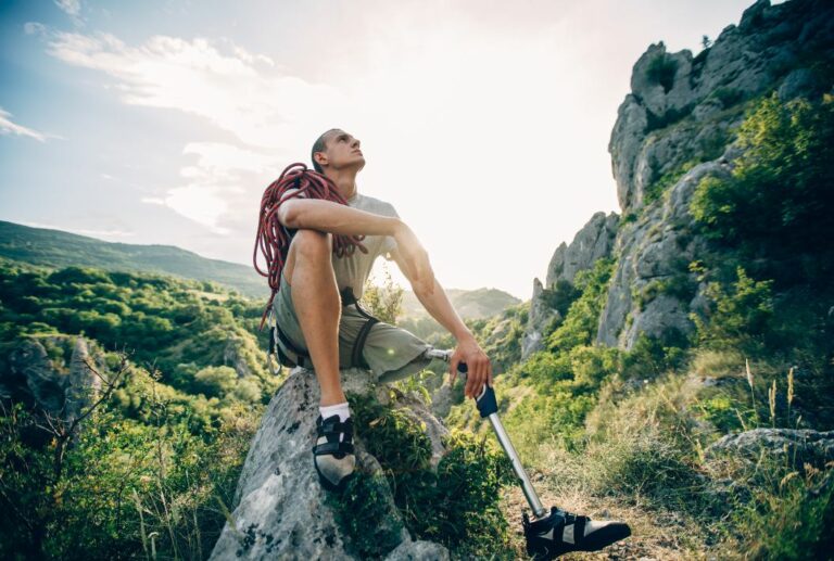 A man with a prosthetic leg sitting on top of a rock after rock climbing.