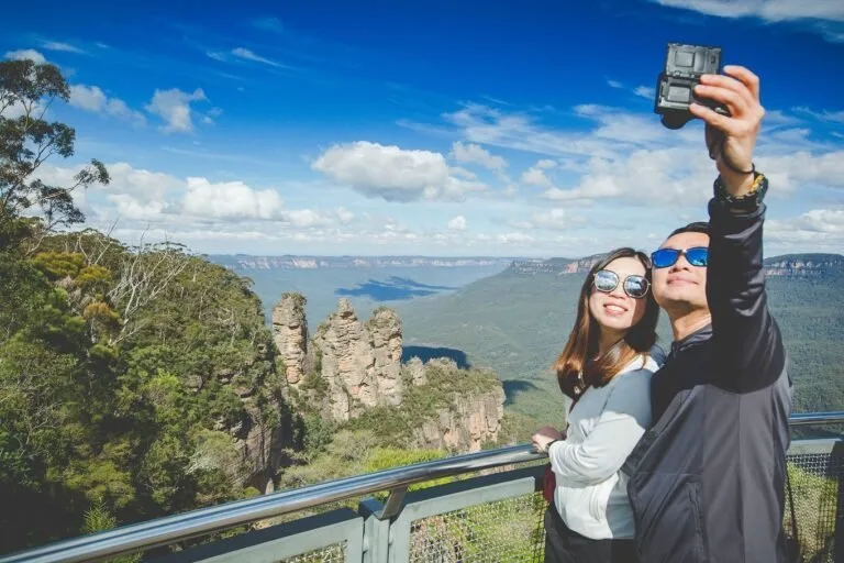 Two tourists taking a selfie at the Three Sisters rock formation in the Blue Mountains.