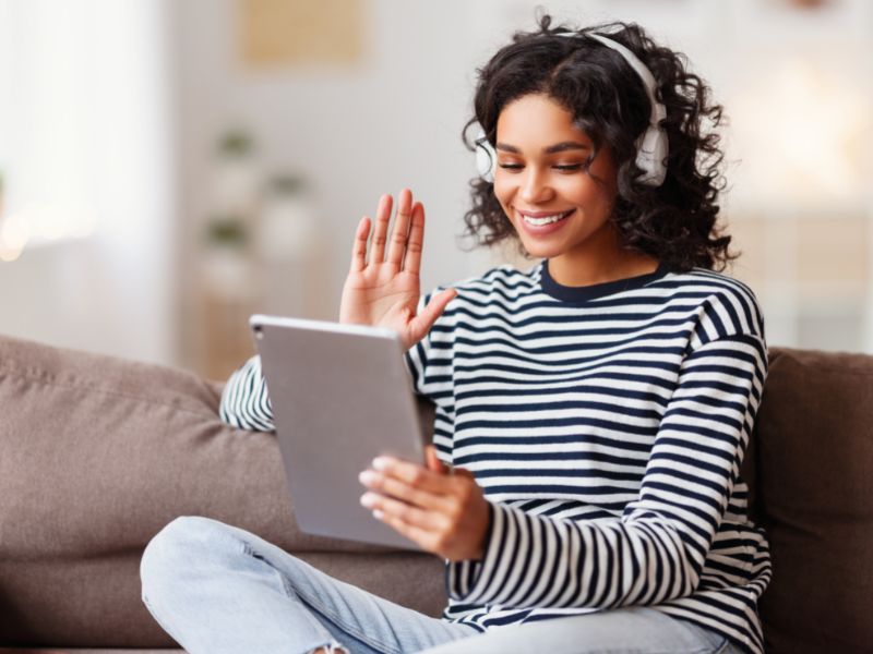 Benefits of a Tourism Tribe Membership - woman sitting on couch on a video call smiling and waving at camera