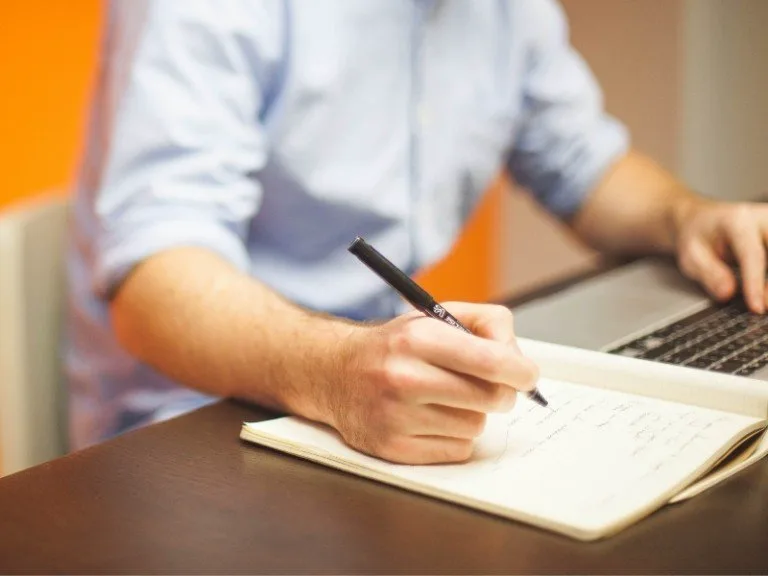 Man at desk writes on notepad