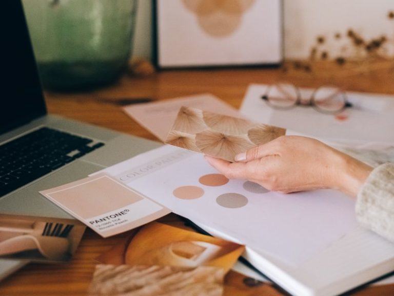 Create a brand style guide in Canva - photo of a womans hand sorting through colour palettes on a desk near a laptop