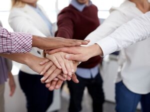 Creating a mentally healthy workplace - photo of hands from 6 people that are stacked on top of one another to celebrate the team