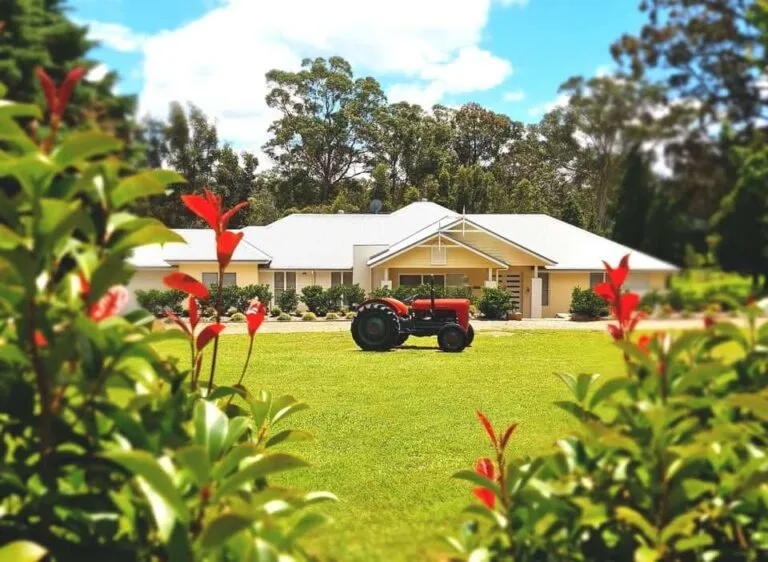 Red vintage tractor parked in front of rural Queensland property with gardens.