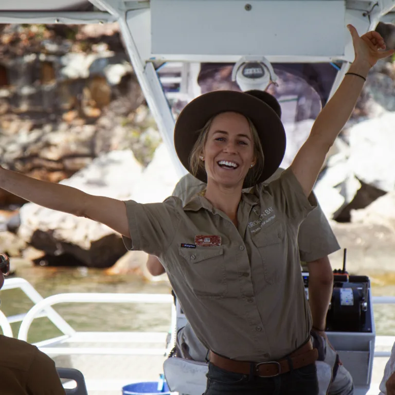 Tourism operator in khaki uniform on boat tour with arms raised in celebration.