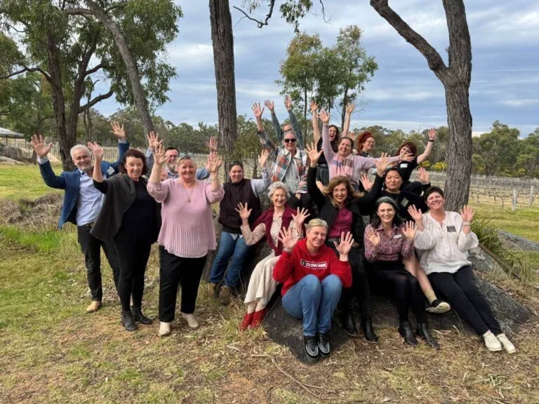 Group of tourism operators waving at camera under tall gum trees in regional Queensland.