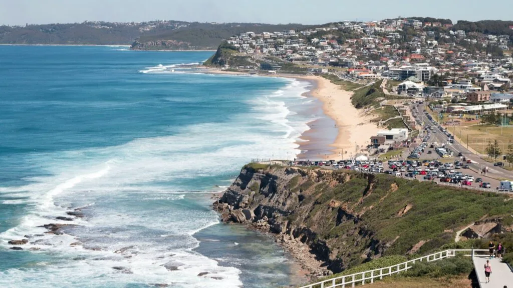 Aerial view of Newcastle beach, NSW, with residential suburbs on headland and ocean swells.