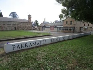 Parramatta Female Factory 1818 memorial sign with historic convict buildings behind.