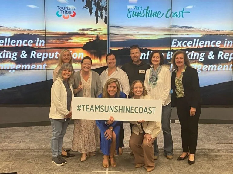 Group of tourism industry professionals holding #TEAMSHINECOAST sign at Sunshine Coast event.
