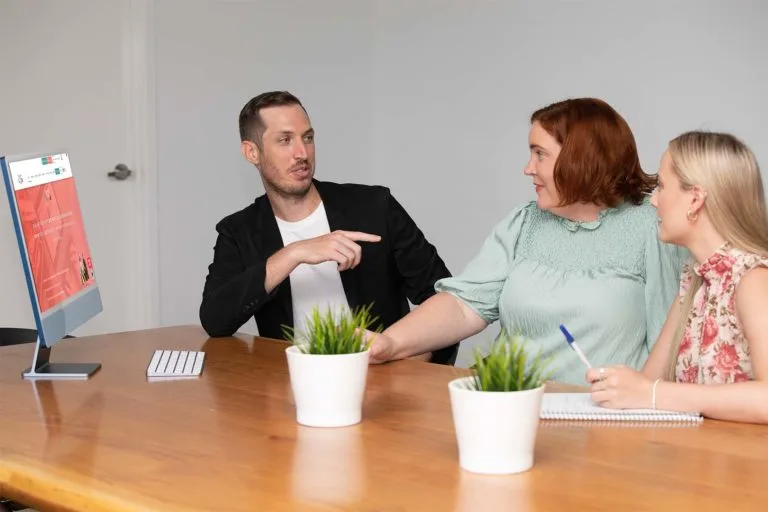 Team members sitting in front of a macbook screen discussing the 20% bonus tax deduction for small businesses under the Small Business Skills and Training Boost
