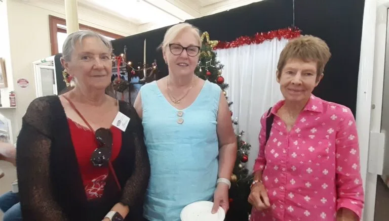 Three women at a Christmas event with festive decorations behind them.