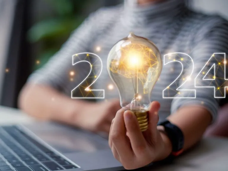Hand holding illuminated lightbulb with 2024 numbers and digital network graphic overlay.