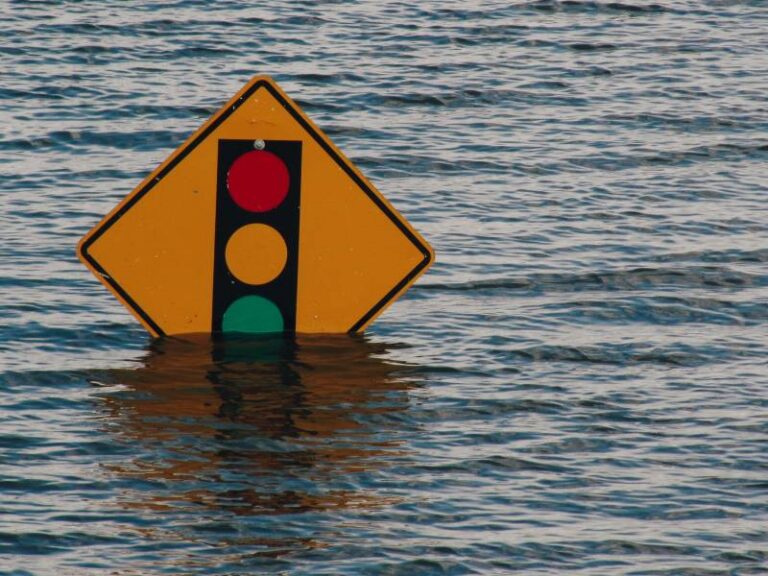 A yellow street lights ahead sign a quarter underwater in a flooded background
