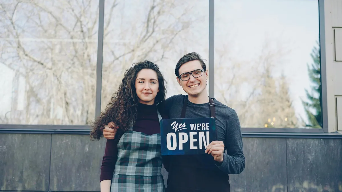 Two smiling small business owners standing outside their shop ready to welcome customers